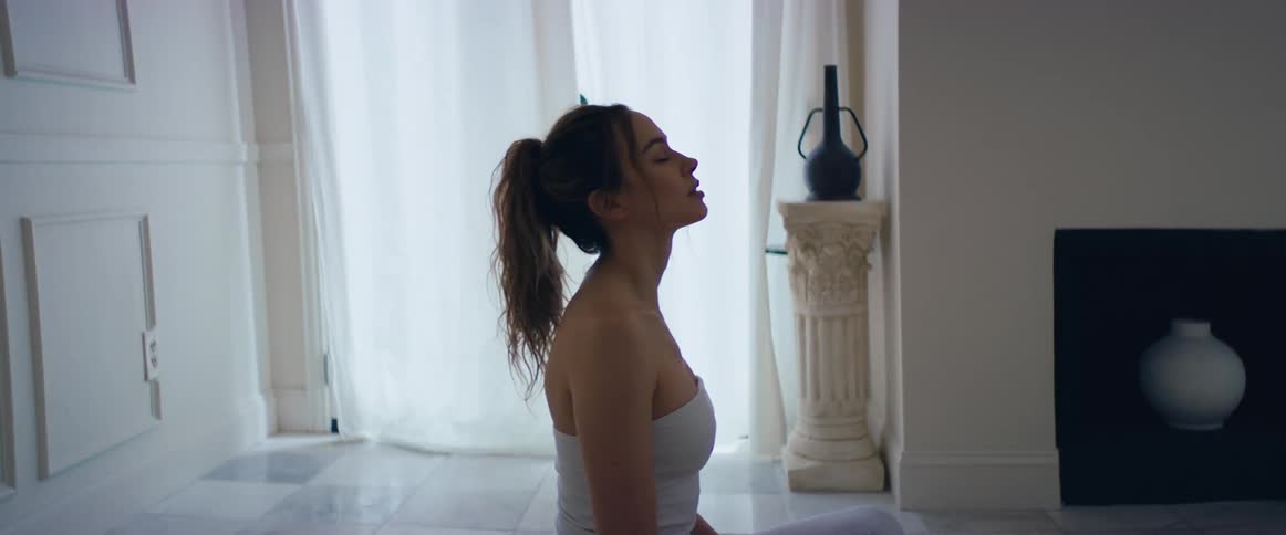 A woman sitting on the floor legs crossed meditating takes a deep breath and stretches her shoulders