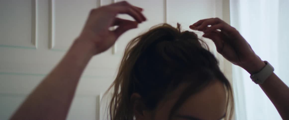 A woman adjusts her hair and stretches her neck and shoulders indoors during the day