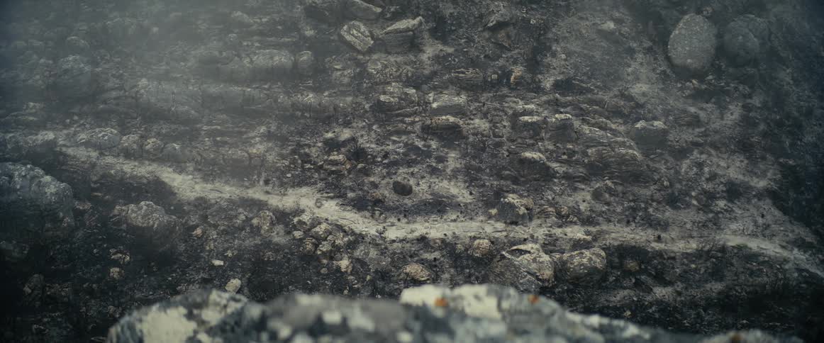 A large mountain of gravel and dirt with rocks is shown with a cloud of smoke passing in front of it
