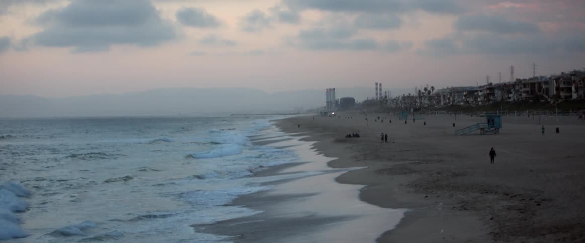 Waves rolling onshore as people mill about the beach on a cloudy evening