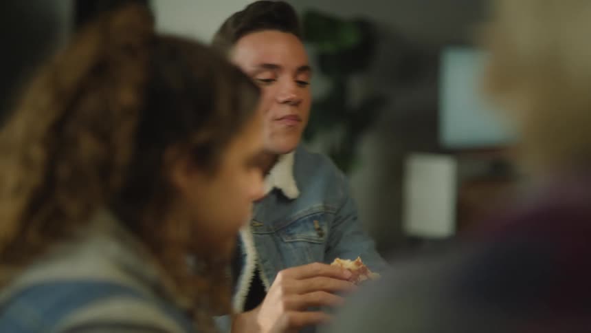 A group of three friends are eating pizza and drinking while laughing and talking