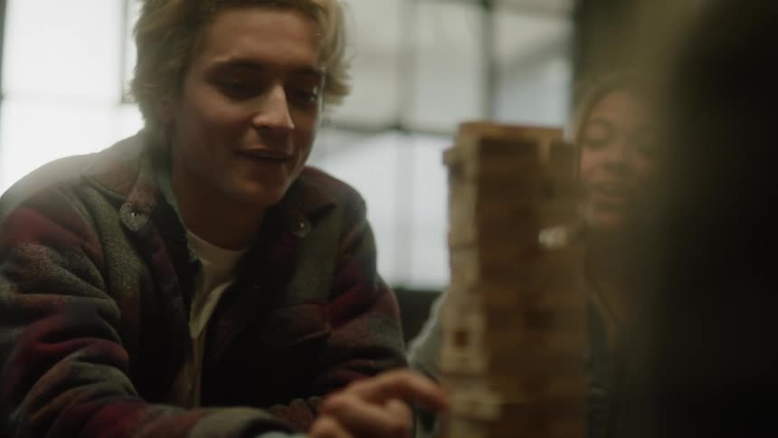 Three friends are indoors playing a game with wooden blocks and laughing