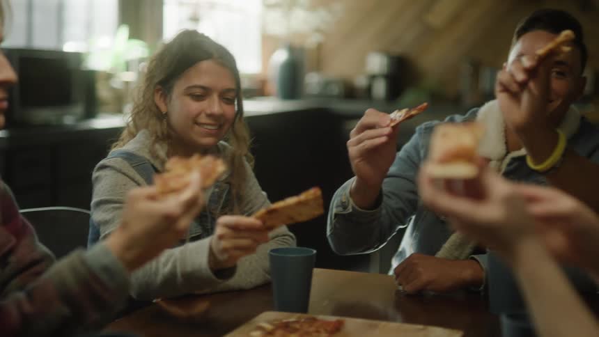 A small group of people are sitting at a table eating pizza in a restaurant as they laugh and talk