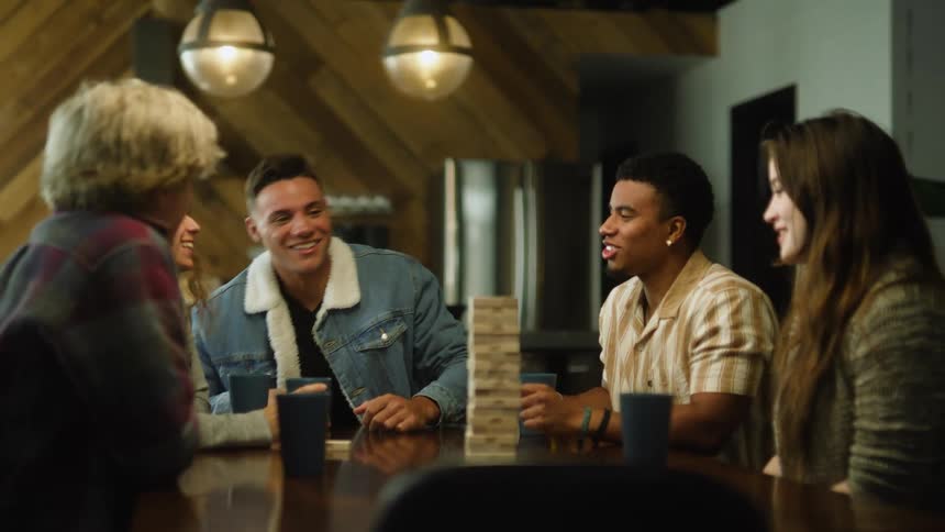 A group of friends is playing a wooden block game sitting at a table