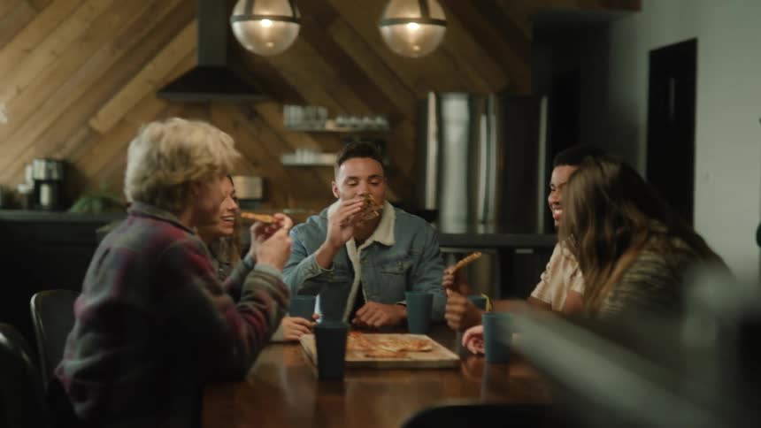 A small group of people are sitting at a table eating pizza in a restaurant as they laugh and talk