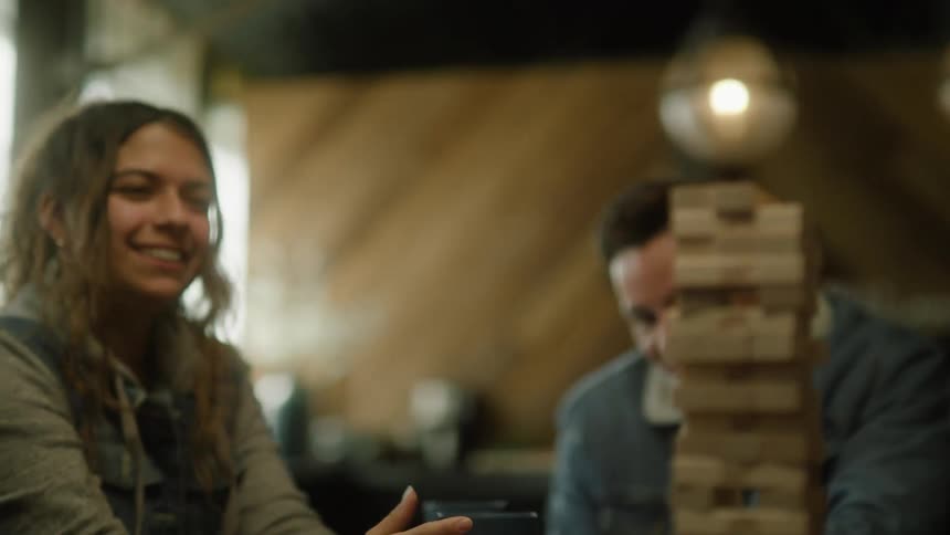 A teenager places a piece on a wooden stacking game while playing with friends in a cafe