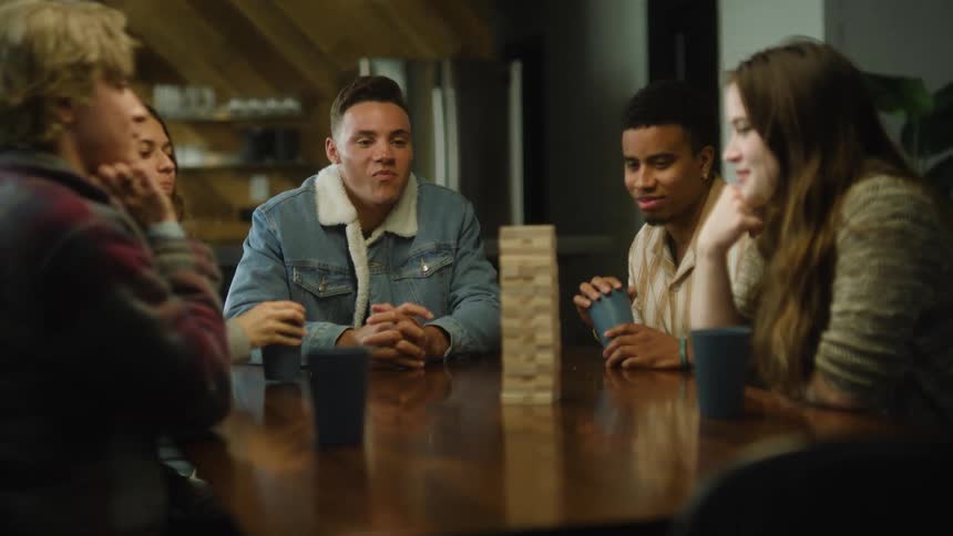 A group of friends think about what to do with a jenga set while they joke around with each other