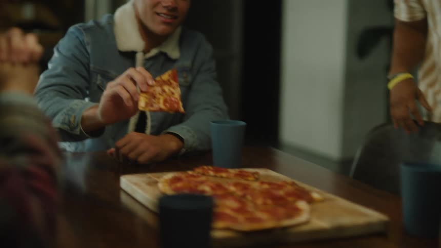 A small group of people are gathered around a table and are starting to eat pizza