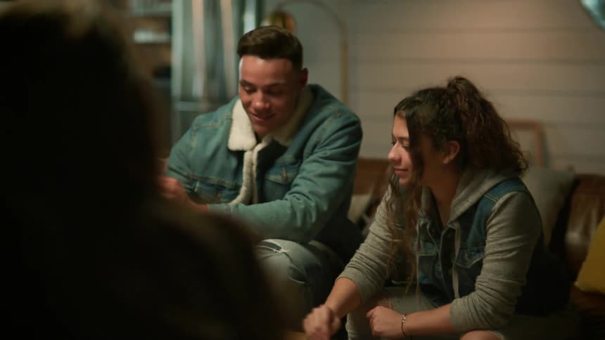 A group of friends sits on couches playing cards and laughing