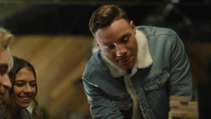 Teenagers laugh at their friend after he knocks over a block stacking game