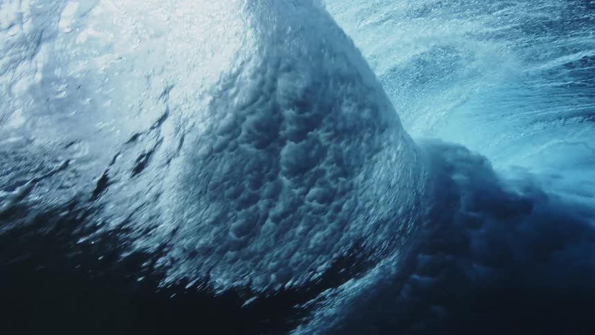 A surfer paddles under a tall wave