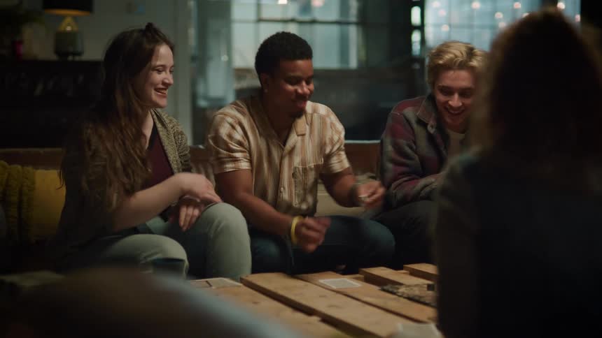 A teenage boy rolls dice in his hands and laughs as he plays a game with his friends