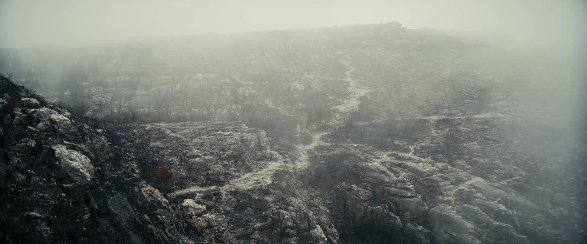 smoke moves over a burnt mountain valley with light ash covering the ground
