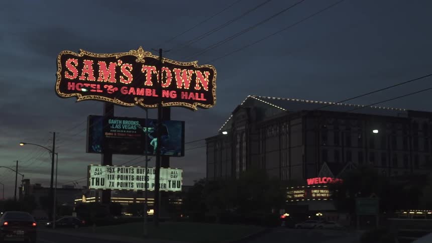 Driving past a bright neon sign for a hotel and casino that stands out against a dusk sky