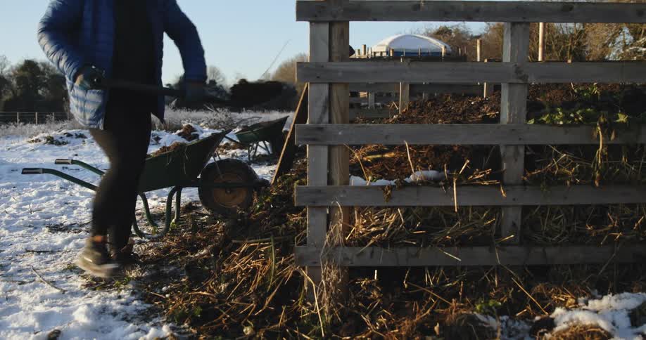 A woman shovels dirt in to a pen on a farm