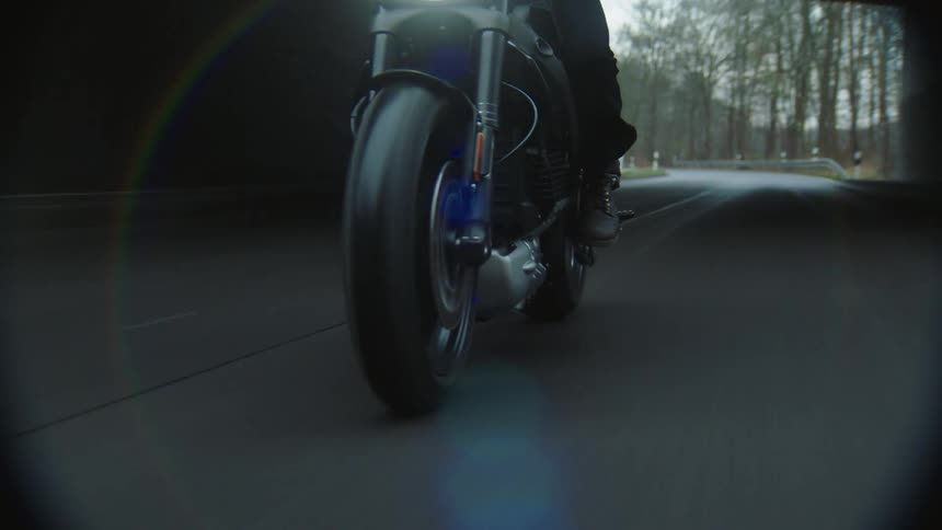 A cyclist is riding a motorcycle on a rural road with trees in the distance as they travel through an overpass