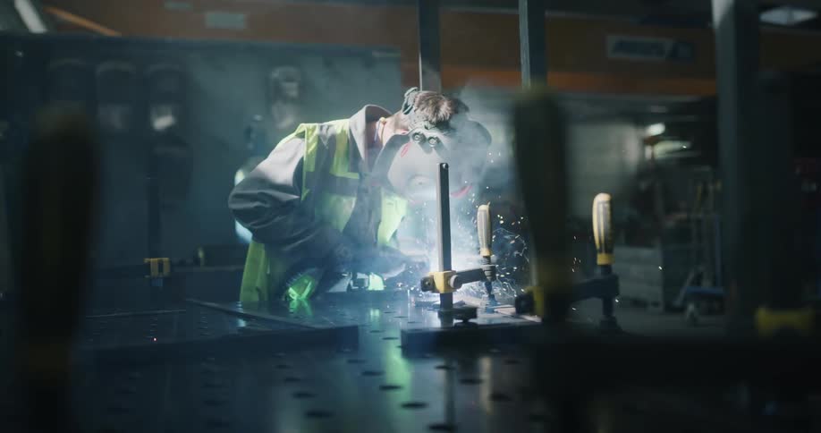 A welder is standing over a work area welding metal as sparks fly