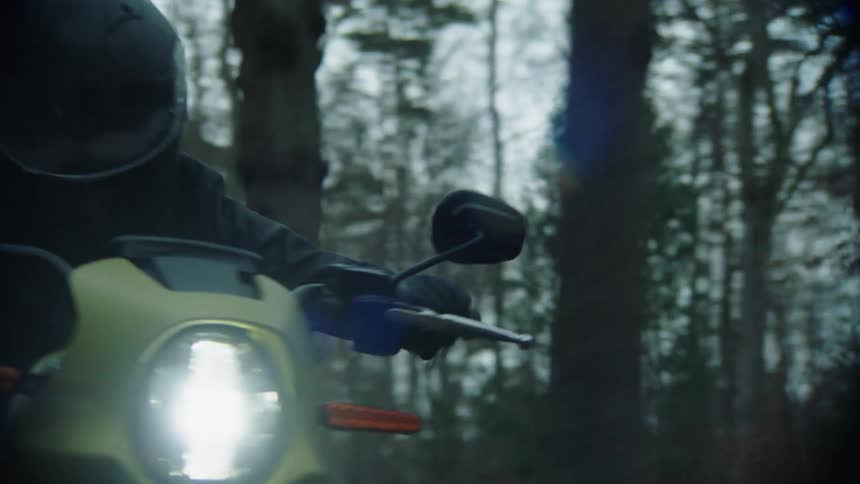 Person wearing a black helmet drives a motorcycle on a road through the forest at evening