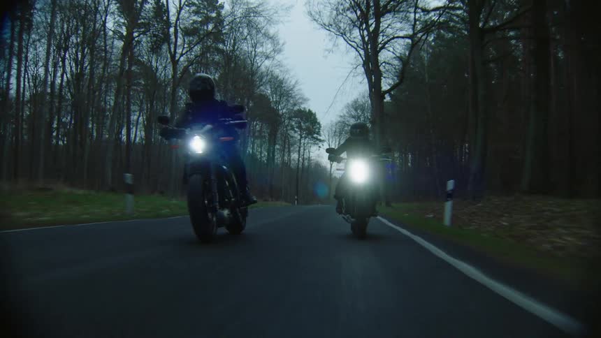 Bikers ride motorcycles on highway in the forest