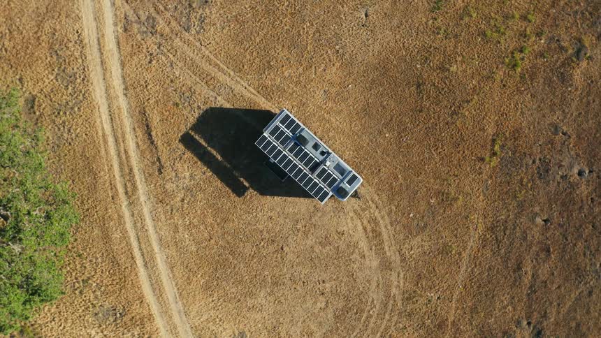 A mobile home with solar panels on the roof is parked on the side of a rural road