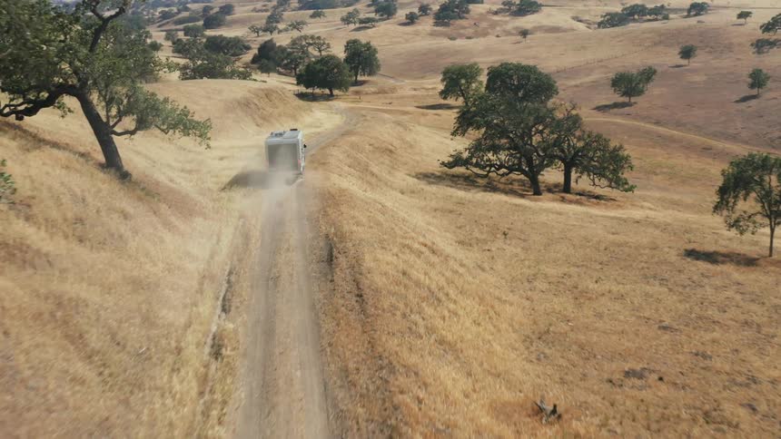 A truck pulls a mobile home along a dirt road through the countryside during the day
