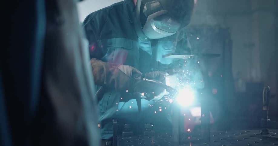 Sparks fly and a bright light glows as a welder is welding metal