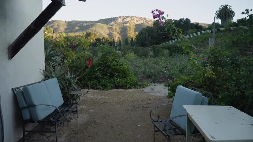 A white fence along the hillside and a mountain in the distance are seen from the patio of a house