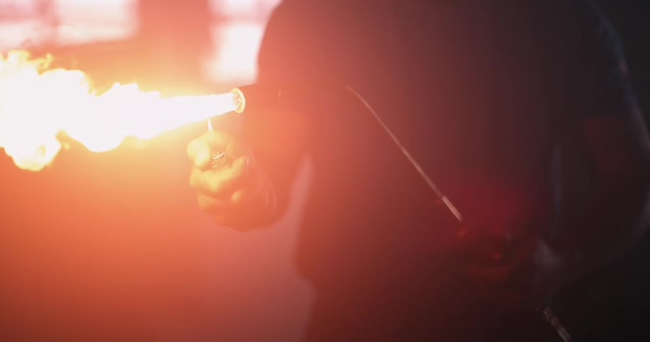 A man is holding a blowtorch as he lights a lighter and a bright flame shoots across the air