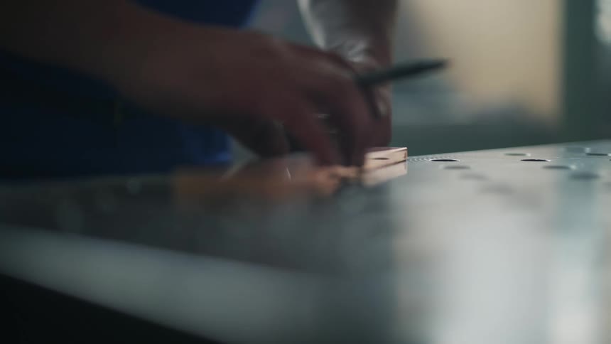 A man is holding a ruler as he measures and marks a piece of wood with a pencil