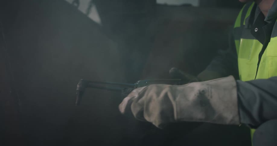 A man wearing gloves and a yellow vest is holding a blowtorch
