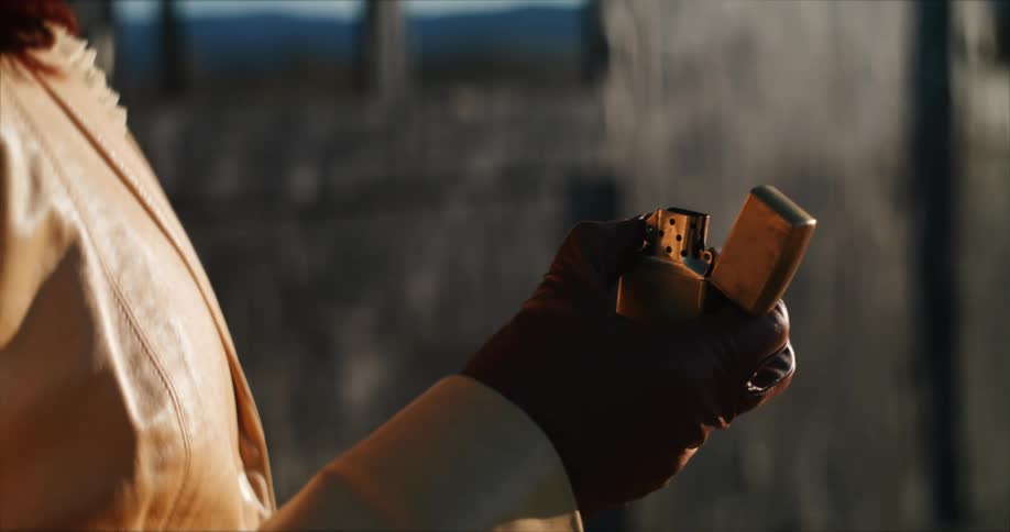 A person wearing dark colored gloves is standing outside and they open a lighter and spark a flame