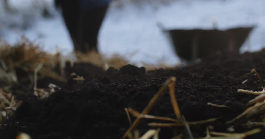 A person shoveling soil onto a pile of straw in winter