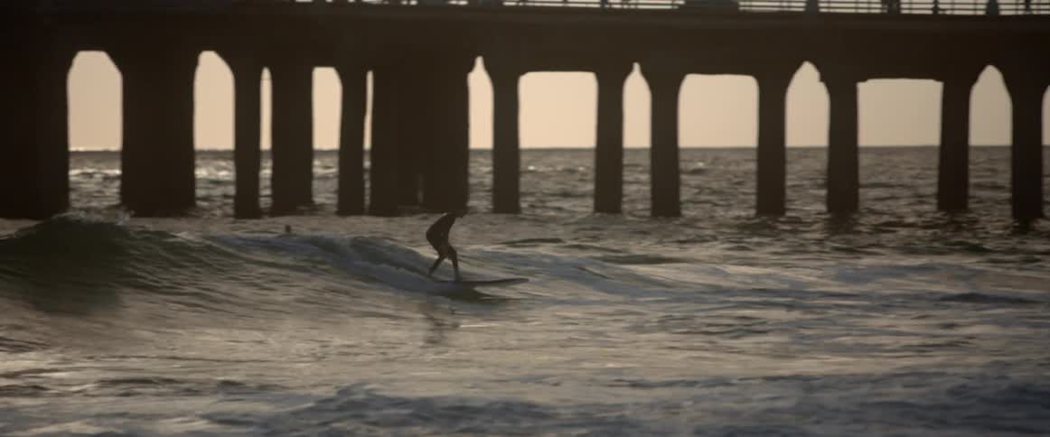 A person surfs near a pier