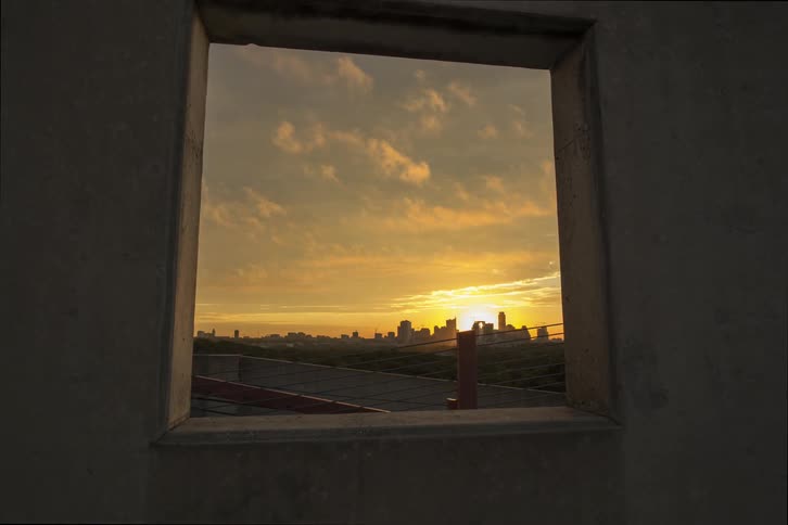 Through a window the sun begins to set