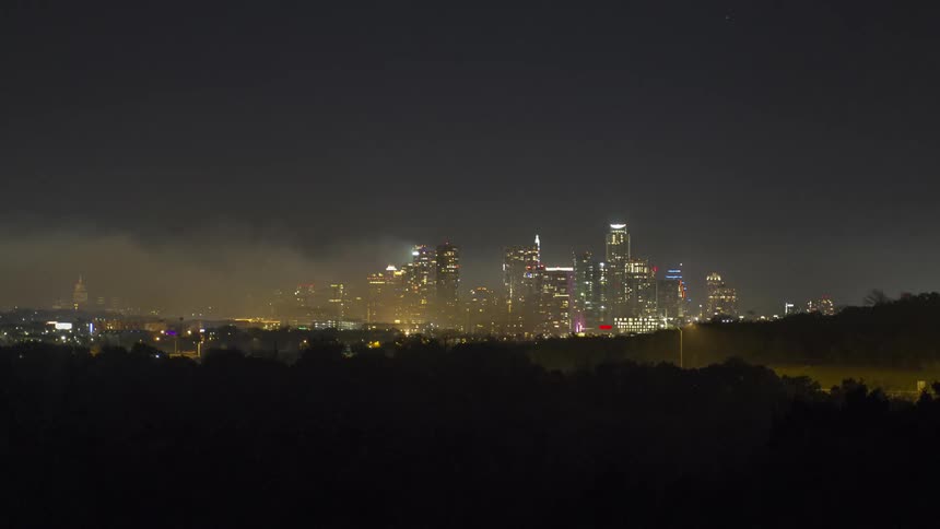 City lights illuminate the night sky as smoke spreads across the city