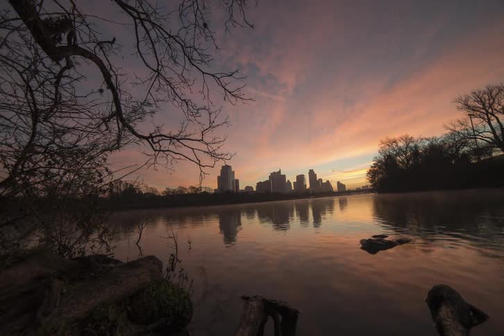 The sun rises over a lake near a city