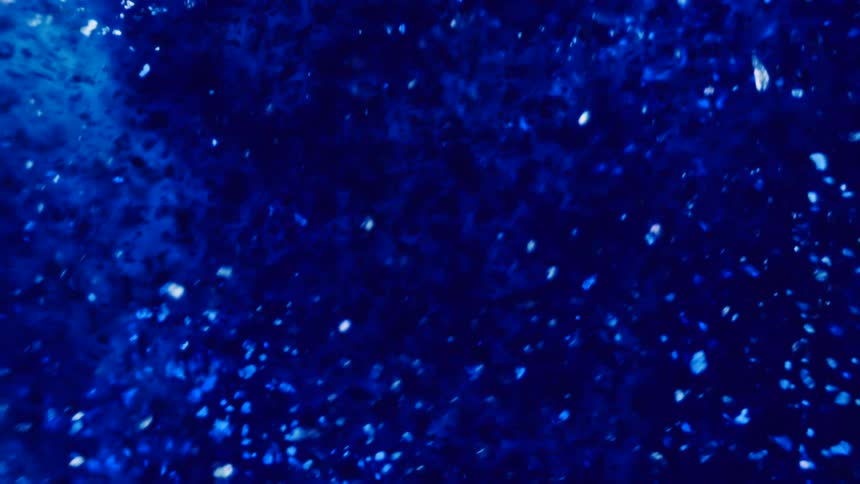 Particles float and swirl in sloshing blue liquid