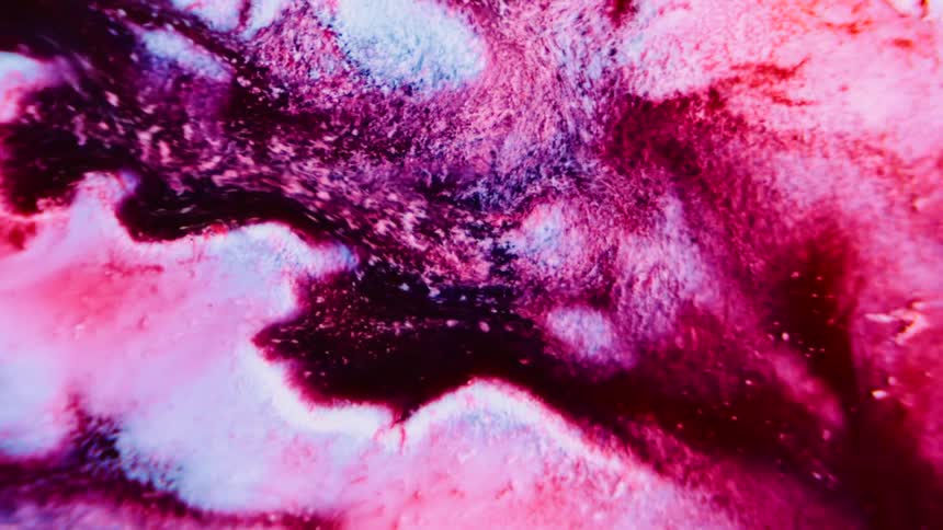 A glowing pink and white substance is breaking apart into particles and flowing in a dark liquid environment
