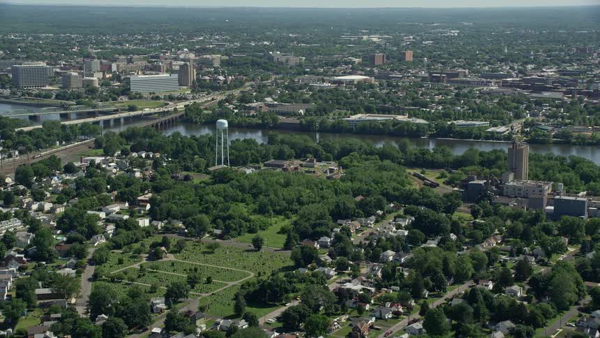 Aerial footage of Morrisville PA and Trenton NJ over residential areas waterways and a cemetery on a sunny day