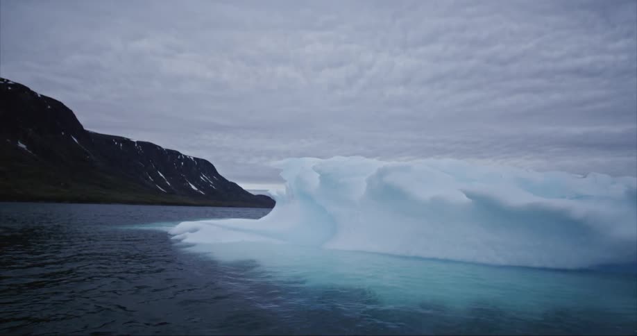 A melting iceberg floats under incoming storm clouds in the arctic sea