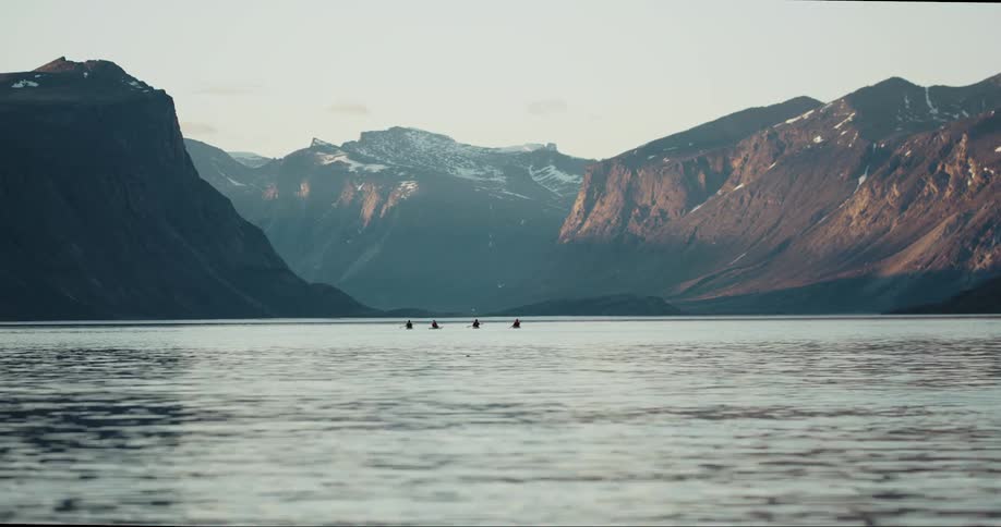 Four people paddle sea kayaks in the arctic sea near baffin island as granite peaks soar above