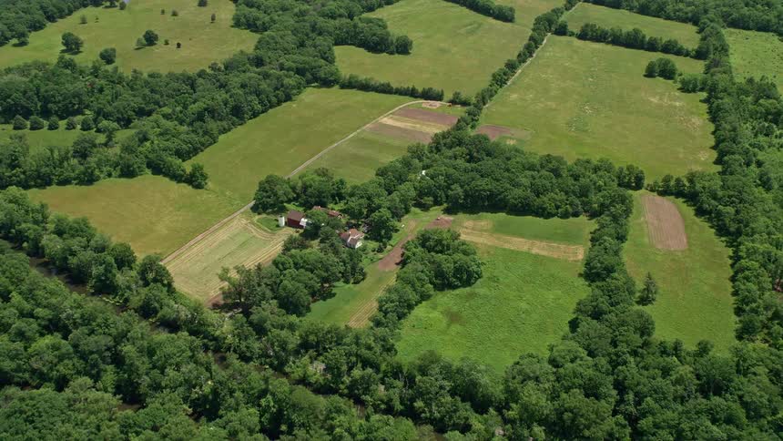 An aerial view shows a rustic farmhouse and barn surrounded by green fields and meadows in Belle Mead New Jersey during summertime