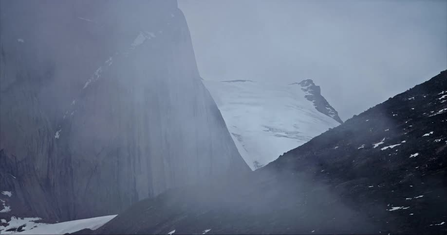 Clouds passing over the snow covered glacier on the slopes of towering granite alpine mountains