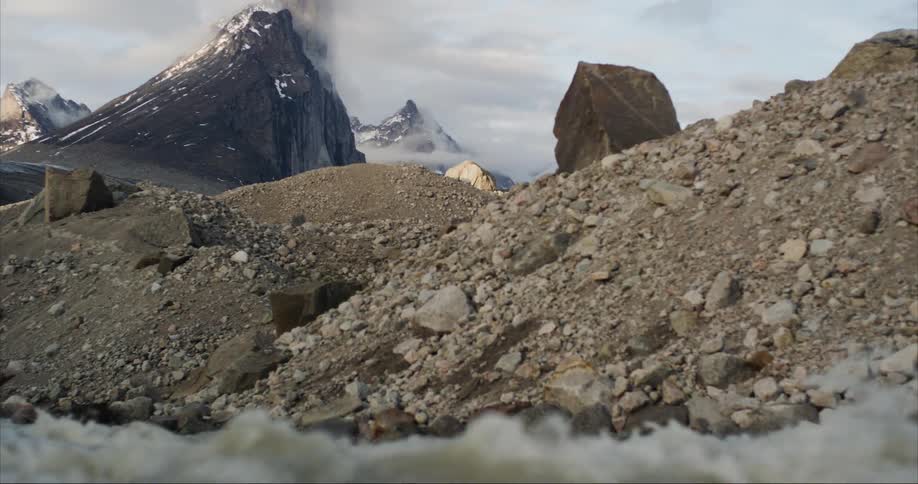A glacier fed river tumbles past a rocky river valley with towering peaks behind
