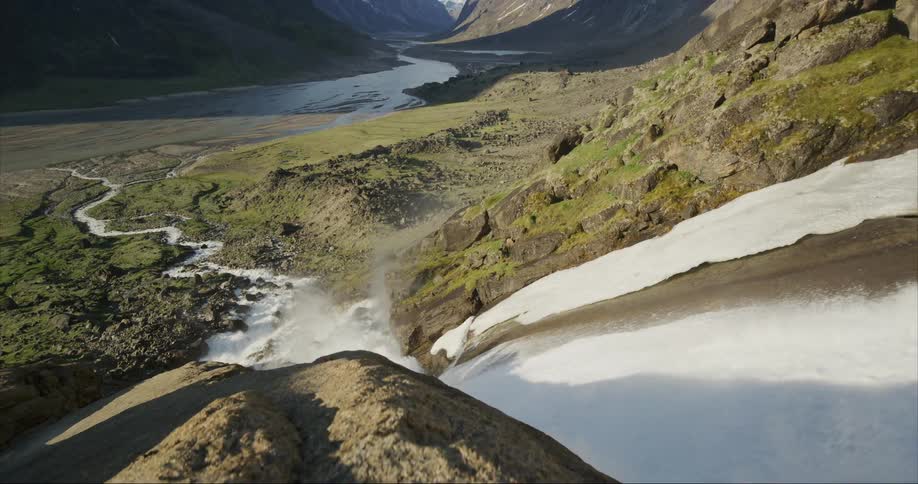 A massive waterfall empties into a stream down the mountain range