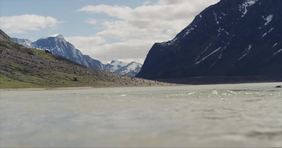 The water flows by glacier covered mountain peaks in the Arctic circle