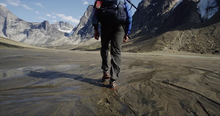 Man carrying a backpack hikes on a glacier valley next to the mountains on Baffin Island in the Arctic Circle