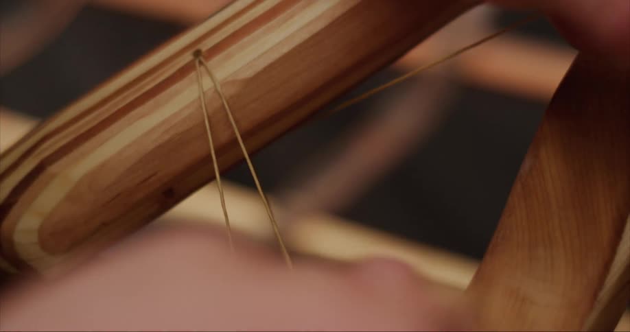 A person is tying a series of knots in a string on a hand built traditional style sea kayak