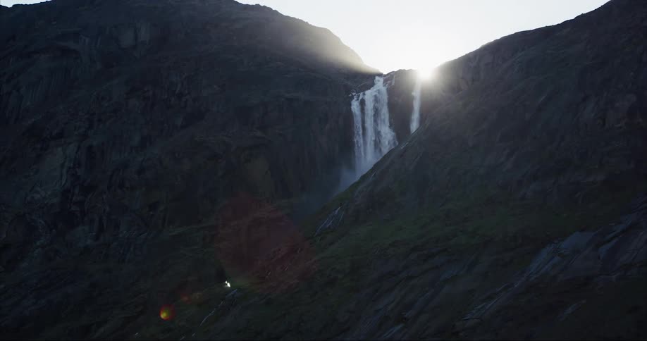 The sun shines above a glacier fed waterfall under the midnight sun on Baffin Island