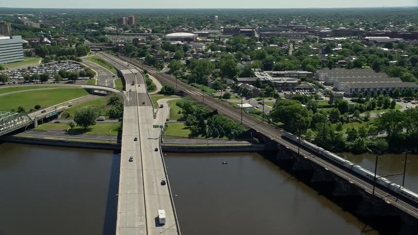Aerial footage of vehicles traveling over a bridge towards the city revealing a commuter train and courthouse in Trenton New Jersey during summer